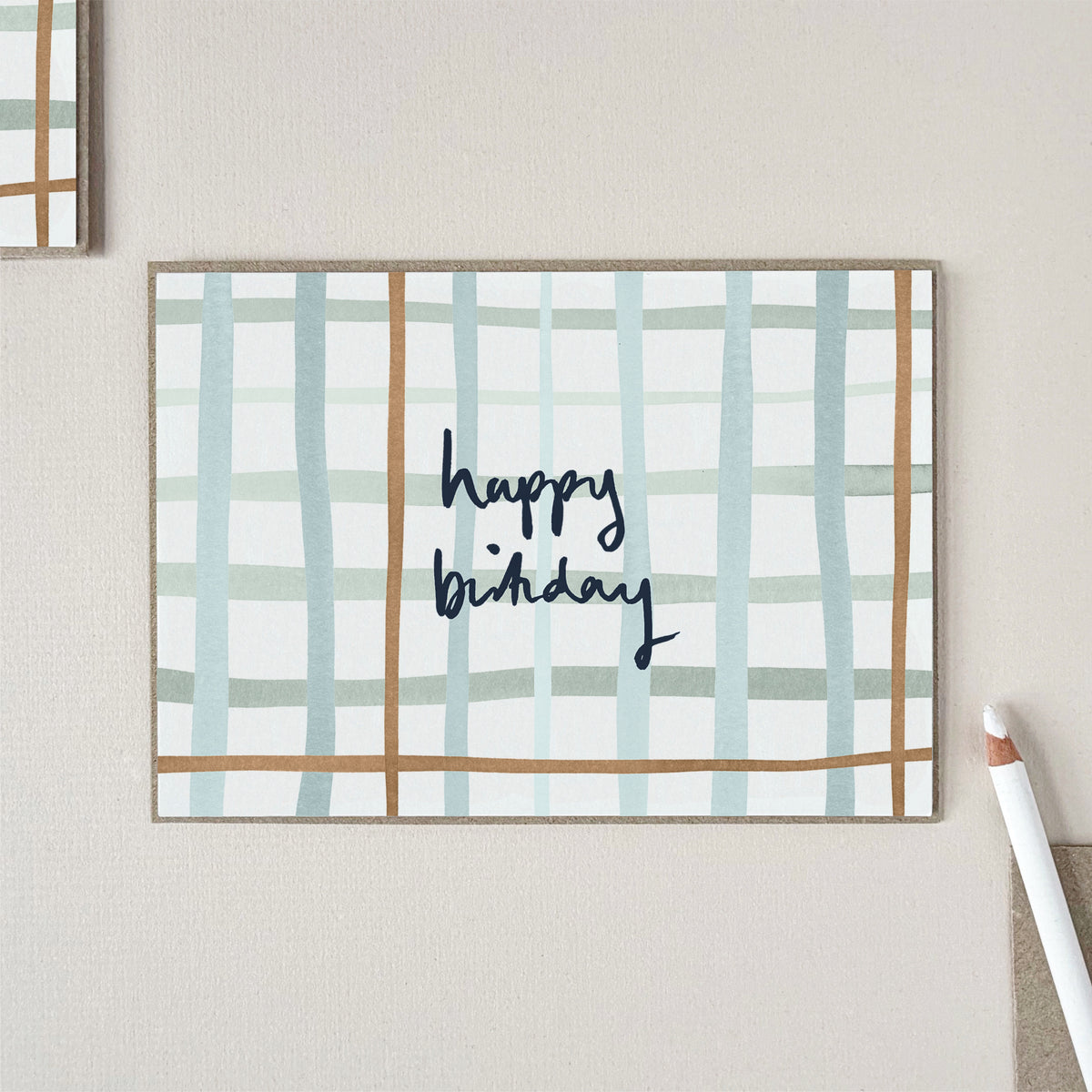 A birthday card with a check pattern in light blue and tan, featuring the words 'happy birthday' in dark blue script.