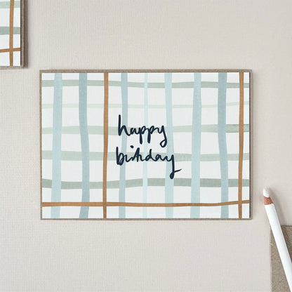 A birthday card with a check pattern in light blue and tan, featuring the words 'happy birthday' in dark blue script.
