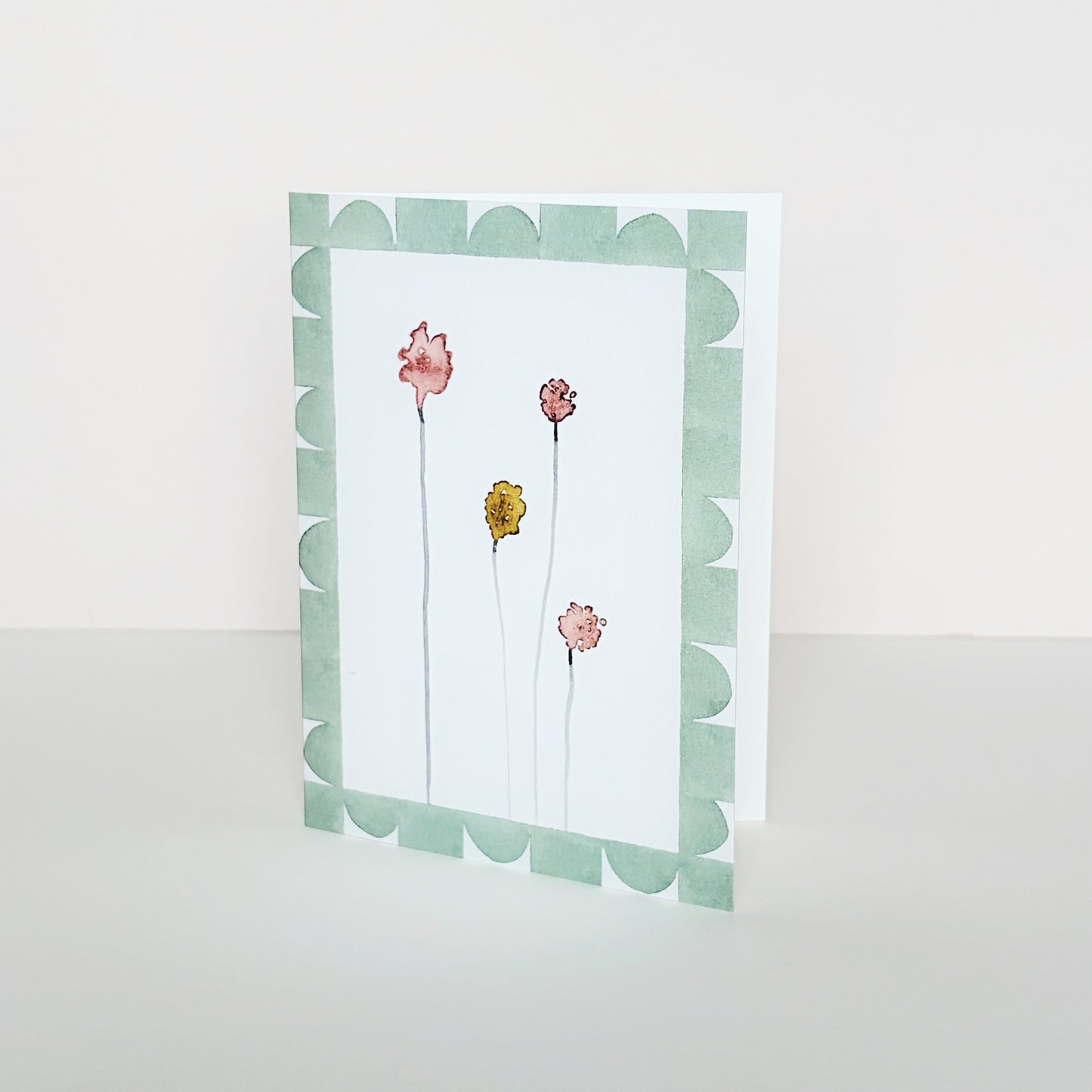 A mini greeting card with a green geometric border around four coloured abstract flower buds.