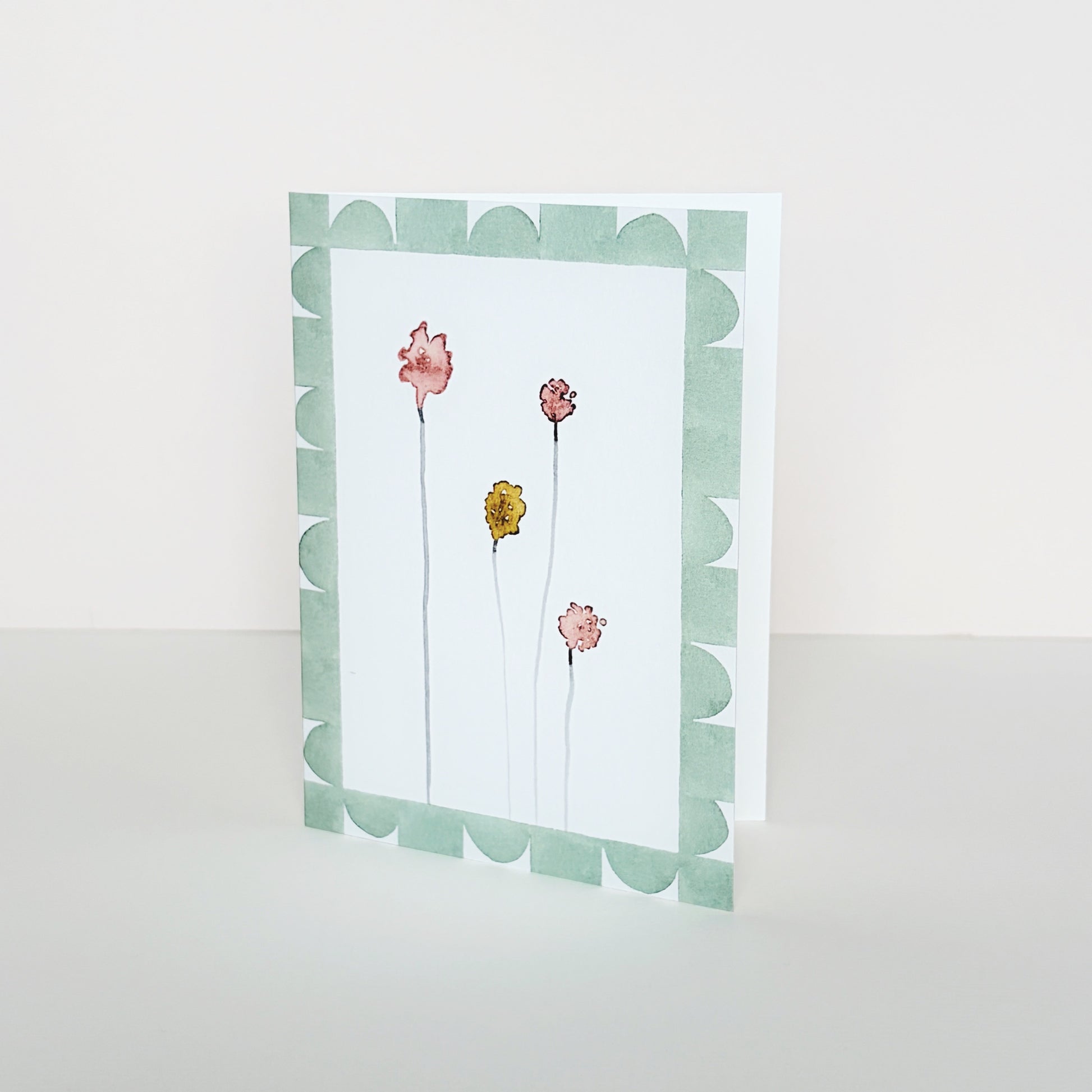 A mini greeting card with a green geometric border around four coloured abstract flower buds.
