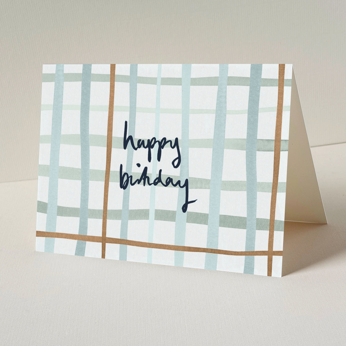 A folded greeting card standing upright, featuring a white background with a check pattern in light blue and tan, and the words 'happy birthday' written in dark blue script.