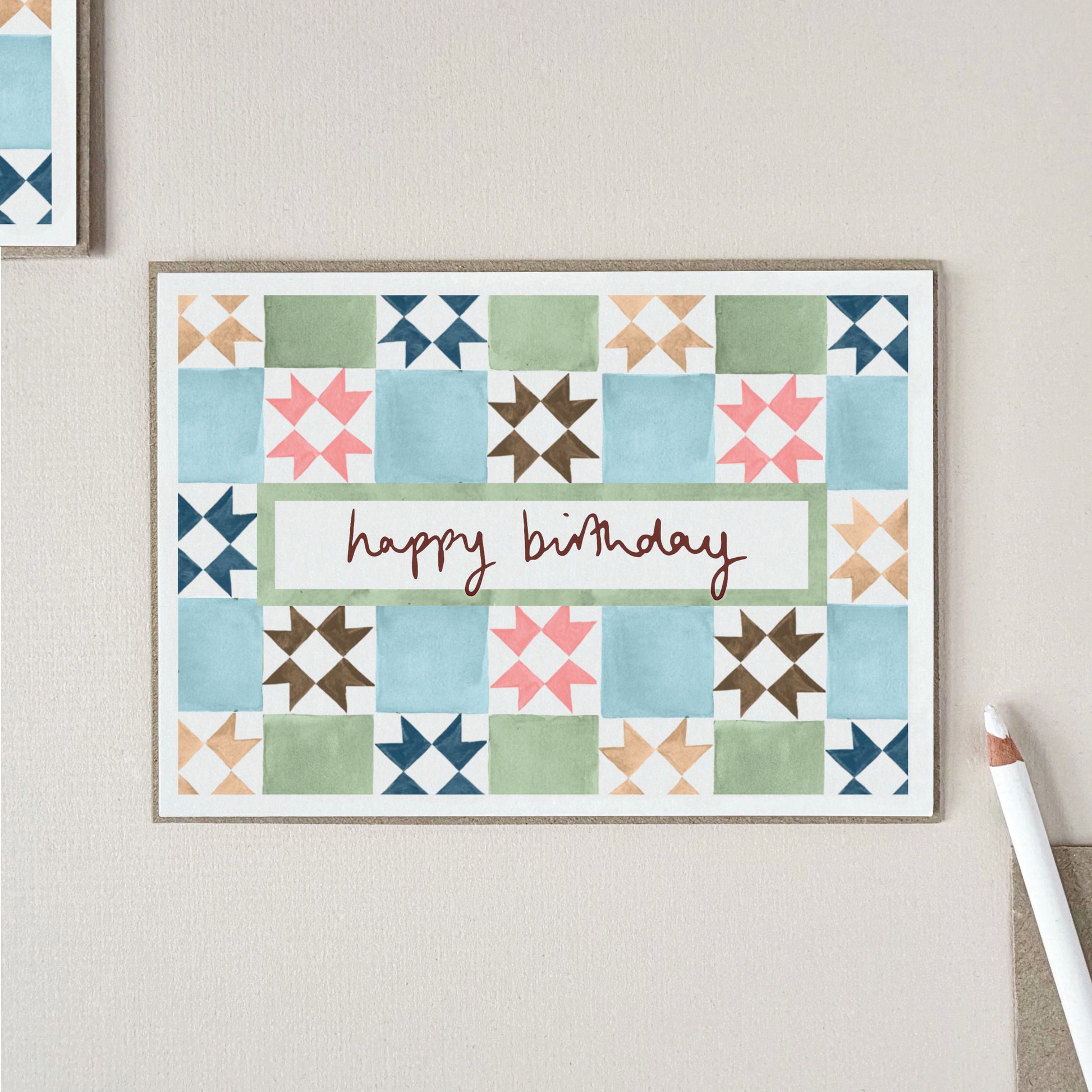 A birthday card with a vintage tile pattern in blue, green, pink, brown, and beige, with the words 'happy birthday' across the center.
