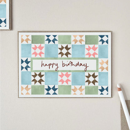 A birthday card with a vintage tile pattern in blue, green, pink, brown, and beige, with the words 'happy birthday' across the center.