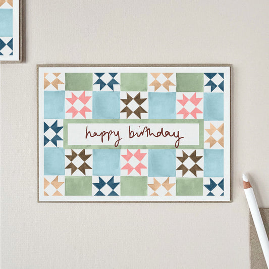 A birthday card with a vintage tile pattern in blue, green, pink, brown, and beige, with the words 'happy birthday' across the center.