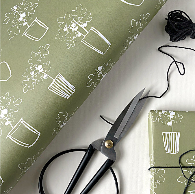Olive green wrapping paper with white plant pattern, scissors, and black thread