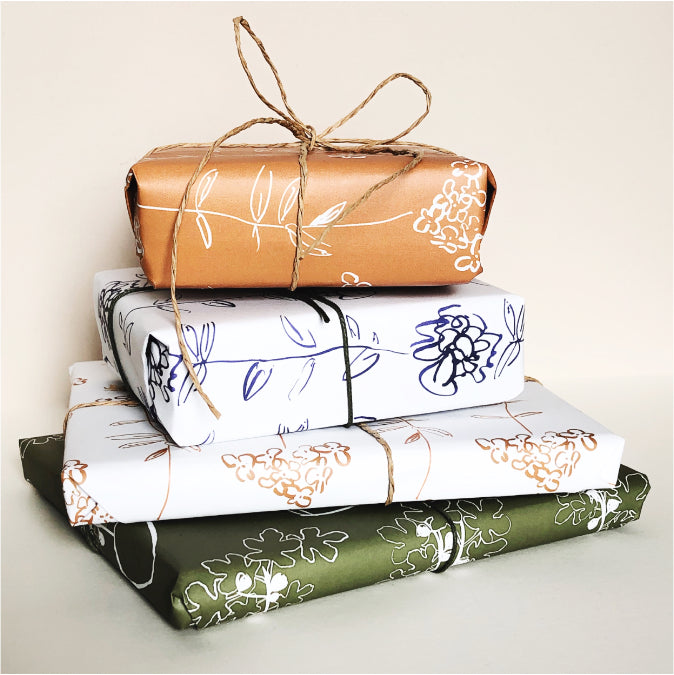 Stack of wrapped gifts in brown, white, and green floral paper on a light background